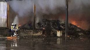 zwei Feuerwehrleute richten Wasserstrahl in eine brennende Halle