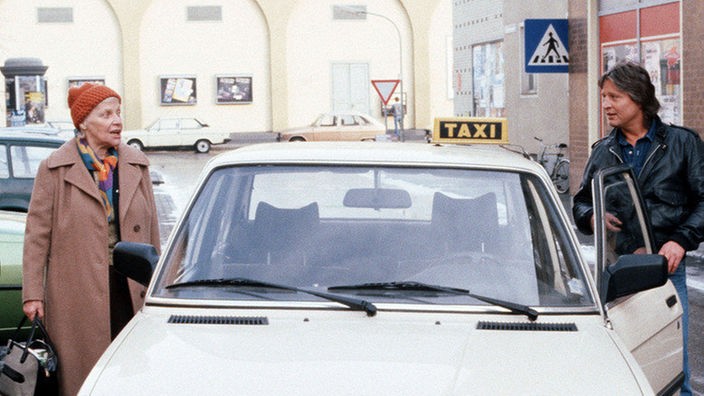 Beinahe hätte Andy (Jo Bolling) seine neue Nachbarin Else (Annemarie Wendl) mit seinem Taxi angefahren.