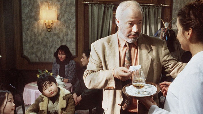 Erich (Bill Mockridge) bittet die Bedienung im "Café Bayer" (Annette Seifert), auf die Kinder (Galia und Sascha Emelin) aufzupassen.