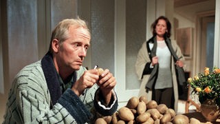 Früh geschält ist halb gewonnen: Hans (Joachim Hermann Luger) bemüht sich mit dem Kartoffelberg, der später Teil des großen Weihnachtsmenüs werden soll. Anna (Irene Fischer) staunt nicht schlecht.