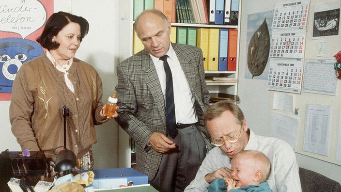 Hans Beimer mit Baby im Büro. Sein Chef wundert sich über die neue Arbeitsmethode.(v.l.: Maria Mittler, Karl-Heinz Gierko und Joachim Hermann Luger)
