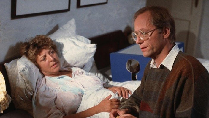 Hans (Joachim Hermann Luger) kümmert sich rührend um die grippekranke Helga (Marie-Luise Marjan).
