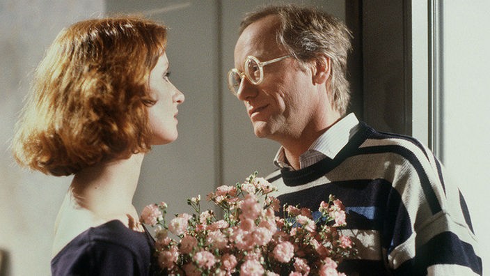 Hans (Joachim Hermann Luger) überrascht Anna (Irene Fischer) nach ihrem Umzug mit einem Blumenstrauß.