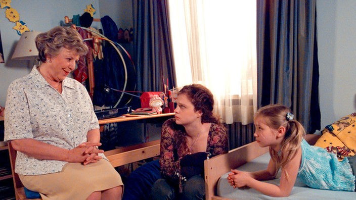 Helga (Marie-Luise Marjan, links) berichtet der entsetzten Nastya (Anja Antonowicz, Mitte), dass sie eine nette Au-pair-Familie für Nastya gefunden hat. Lea (Anna Sophia Claus) ist dagegen, dass ihre Freundin wegziehen soll.