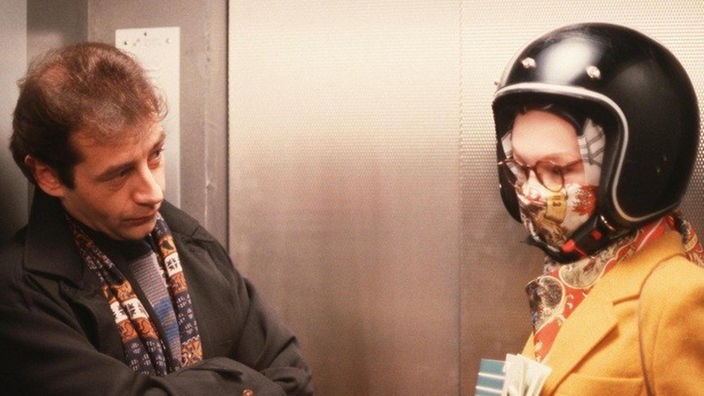 Im Fahrstuhl trifft Nossek (Dietrich Siegl) auf Chris (Stefanie Mühle), die sich für die nächste Demo einen Helm gekauft hat.