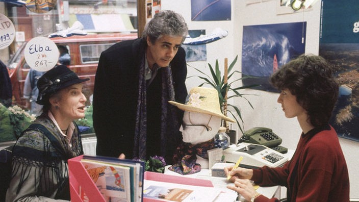Jean-Luc (Gerard Herold) besucht seine Tochter Dominique (Brigitte Annessy) an ihrem Arbeitsplatz in einem Reisebüro.