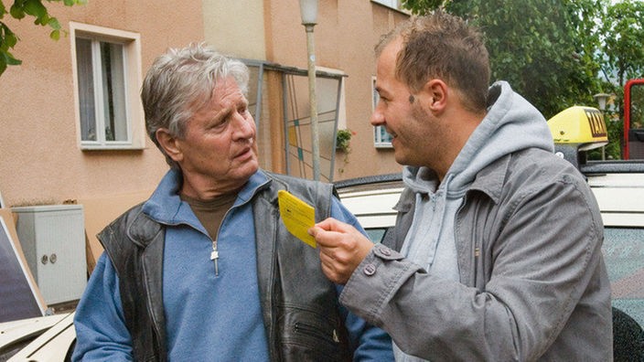 Olli (Willi Herren, rechts) überrascht Andy (Jo Bolling) mit dem Taxischein. So können sich die beiden die Schichten nun teilen.