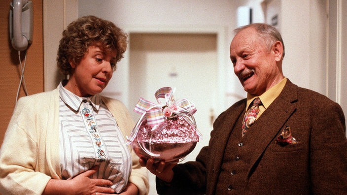 Onkel Franz (Martin Rickelt) schenkt Helga (Marie-Luise Marjan) ein großes Schokoladenei.
