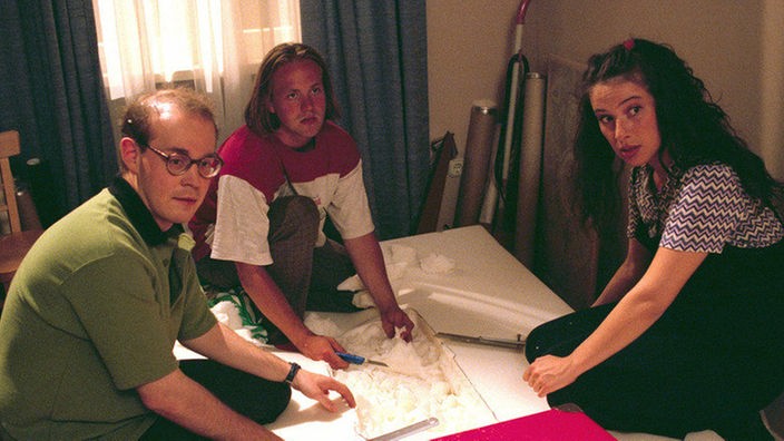 Philipp (Philipp Neubauer, li), Klaus (Moritz A. Sachs) und Dani (Clelia Sarto) befassen sich konzentriert mit dem roten Koffer.