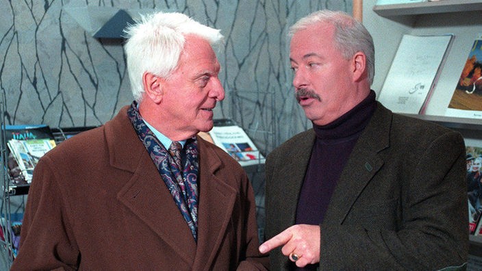 Priesnitz (Carlos Werner, links) lässt sich von Erich (Bill Mockridge) im Reisebüro beraten.