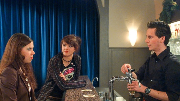 Sarah (Julia Stark, links) hat sich in den jungen Kellner Fabian (Roman Haubner) verliebt. Jack (Cosima Viola) hilft dem jungen Glück auf die Sprünge.