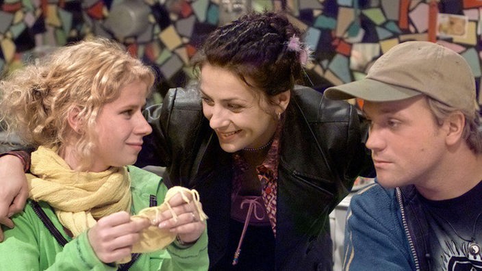 Suzanne (Susanne Evers, Mitte) freut sich, dass ihre Mitbewohner Nina (Jacqueline Svilarov) und Klaus (Moritz A. Sachs) aus dem Urlaub zurück sind.