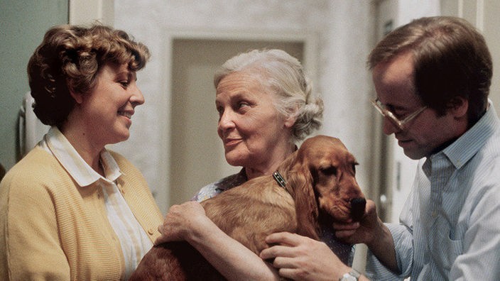 Was macht Else Kling (Annemarie Wendl, Mitte) mit Hund Beimer? Helga (Marie-Luise Marjan) und Hans Beimer (Joachim Hermann Luger) nehmen ihn in Empfang.