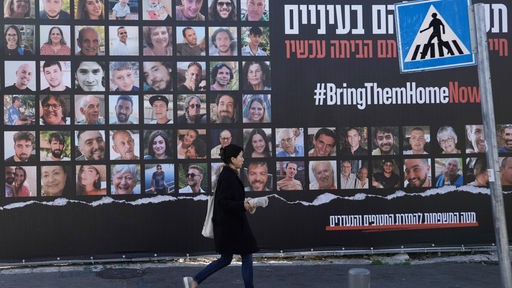 24.11.2023, Israel, Jerusalem: Eine Frau geht in Jerusalem an einem Plakat vorbei, das die Rückkehr von etwa 240 Geiseln fordert, die während des Hamas-Angriffs auf Israel am 7. Oktober entführt worden waren.