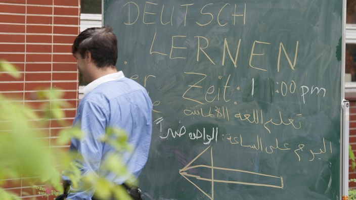 Mann vor einer Tafel mit der Aufschrift Deutsch lernen