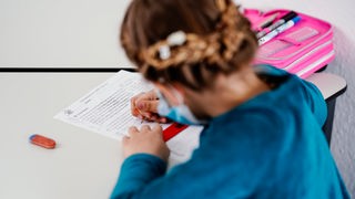 Ein achtjähriges Mädchen sitzt in einer Nachhilfeschule während einer Deutschstunde an einem Tisch vor einem Übungsblatt.