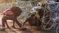 Männer kriechen durch einen Grenzzaun aus Stacheldraht