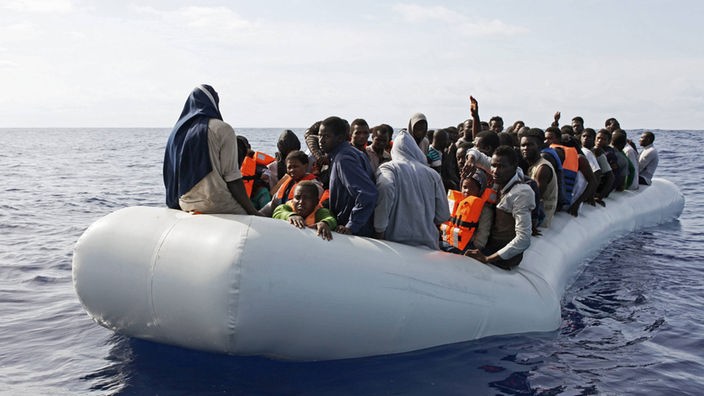 Eine Gruppe von Flüchtlingen treibt auf dem Meer in einem Schlauchboot.