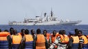 Eine Gruppe von Flüchtlingen auf einem kleinen Boot vor einem Schiff der Marine