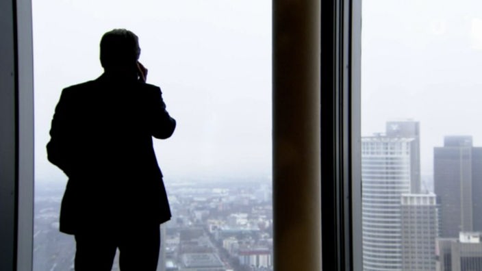 Der Schatten eines Mannes mit Mobiltelefon in einem Büro mit Blick auf Hochhaustürme