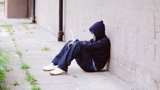 Jugendlicher sitzt an eine Wand gelehnt auf dem Boden