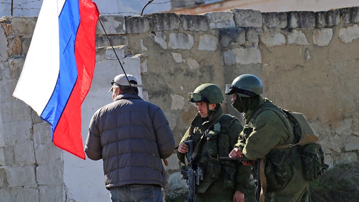 Mann mit russischer Fahne und zwei Soldaten in Uniformen ohne Abzeichen auf der Krim