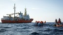 Ein Boot mit Flüchtlingen schwimmt vor der libyschen Küste neben dem Seenotrettungsschiff Aquarius 2.