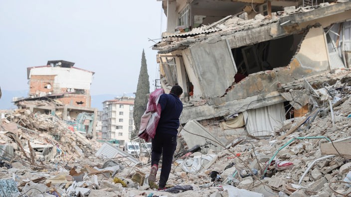 Ein Blick auf die vom Erdbeben zerstörte Stadt Antakya. Ein Mann mit Tasche geht durch die Ruinen in Richtung einer Zypresse. 