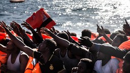 Flüchtlingsdrama im Mittelmeer: Flüchtlinge auf einem Boot recken die Hände, um gerettet zu werden. 
