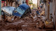 Das Bild zeigt eine Straße nach dem Hochwasser in Valencia. Die Straße ist voller Schlamm und Autos sind aufgetürmt vom Wasser.