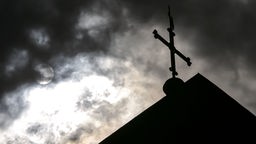 Das Bild zeigt ein Kirchenkreuz vor dunklen Wolken.