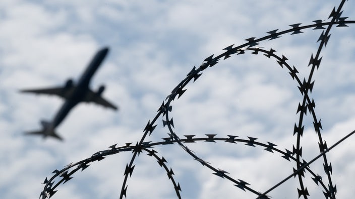 Ein Flugzeug hebt am Flughafen BER hinter einem Zaun mit Natodraht ab (Symbolfoto).