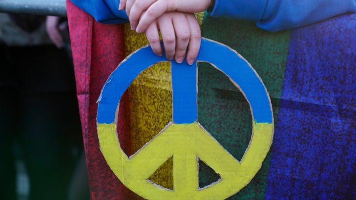Ukraine-Krieg: Pazifismus am Ende? - Besucher:in mit einem Friedenszeichen in den Farben der Ukraine.