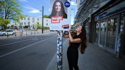Eine Kandidatin bringt ein Wahlplakat an