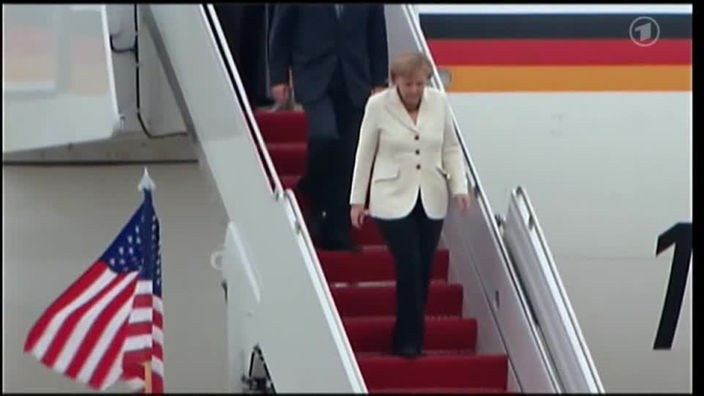 Angela Merkel steigt aus einem Flieger und geht eine Treppe mit rotem Teppich runter