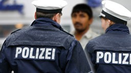 Zwei Polizisten stehen einem Mann mit dunklerer Hautfarbe gegenüber