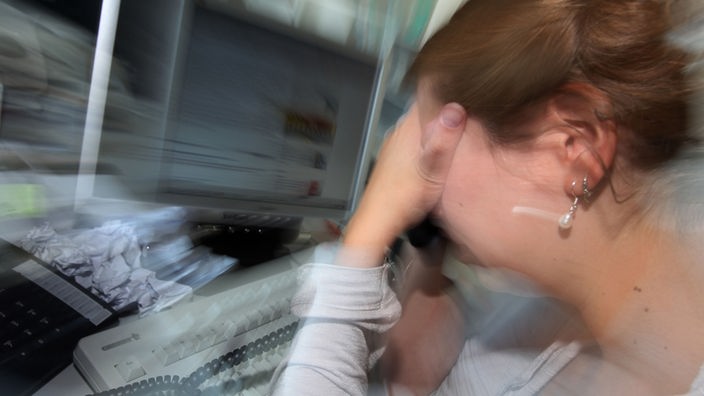 Symbolfoto: Eine depressiv anmutende Frau sitzt an ihrem Arbeitsplatz vor einem Computer