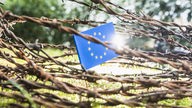 Symbolbild für die Abgrenzung Europas: Flagge der Europäischen Union hinter Stacheldraht