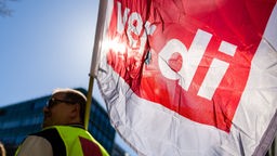 Ein Teilnehmer einer Kundgebung anlässlich des Warnstreiks mit Flagge der Gewerkschaft ver.di.