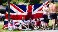 Englische Fußballfans schützen sich in der Kölner Innenstadt im Schatten einer Flagge vor der Sonne