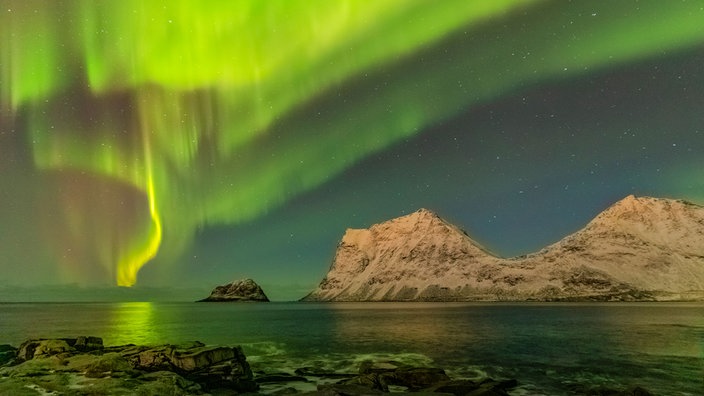 Grüne Nordlichter erhellen einen See und Berge.