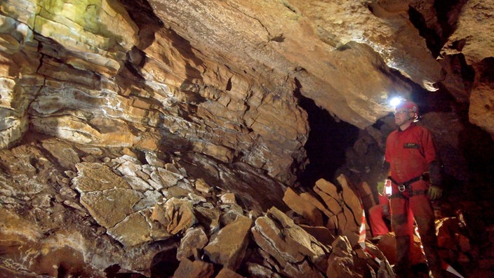 Das Innere eine Höhle mit Höhlenforschern. Man sieht die schichtweise Formation des Gesteins.