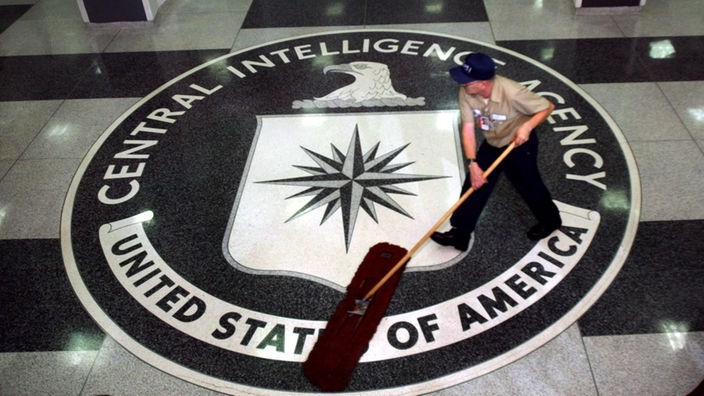 Mann säubert mit einem Wischmop ein in den Fußboden eingelassenes Wappen der CIA