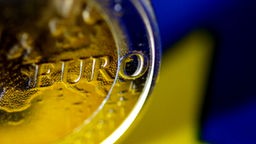 Eine Euromünze vor einem der goldenen Eurosterne der Flagge der EU