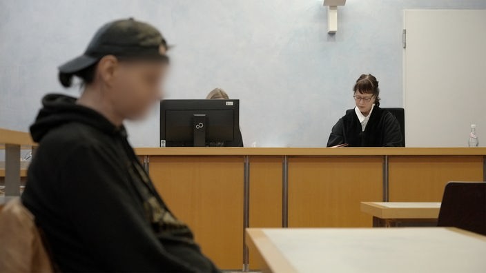 Mann sitzt mit geblurrten Gesicht vor der Richterin