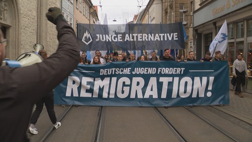 Menschen demonstrieren mit einem Plakat auf welchem steht: "Deutsche Jugend fordert Remigration!"