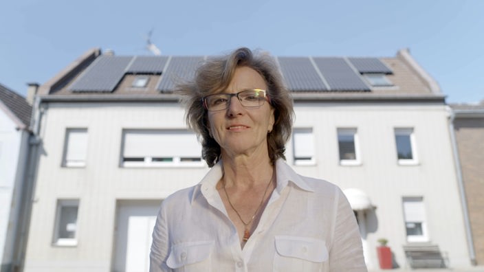 Eine Frau steht vor dem Haus mit Photovoltaik-Anlagen.