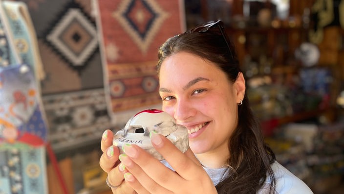 Eine Souvenirverkäuferin mit einer Souvenir in Bunkerform in der Hand.