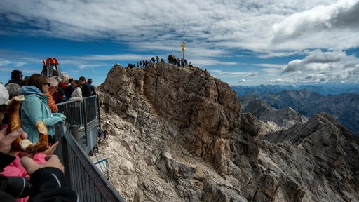 Gipfelkreuz auf den Alpen umgeben von vielen Menschen und einer weiten Aussicht