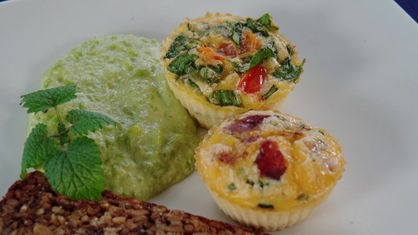 Das Bild zeigt fertige Eier-Muffins mit Käse und Bacon und Tomate, Feta und Basilikum.